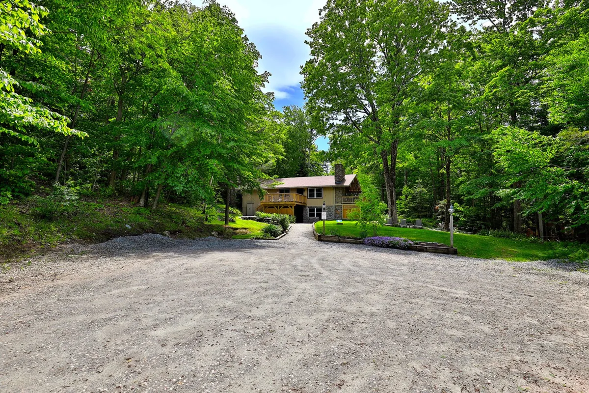 This exterior photo presents the house nestled among trees, with a gravel driveway leading up to it. The serene setting highlights the home as both a private retreat and a convenient base for exploring nearby hotspots.