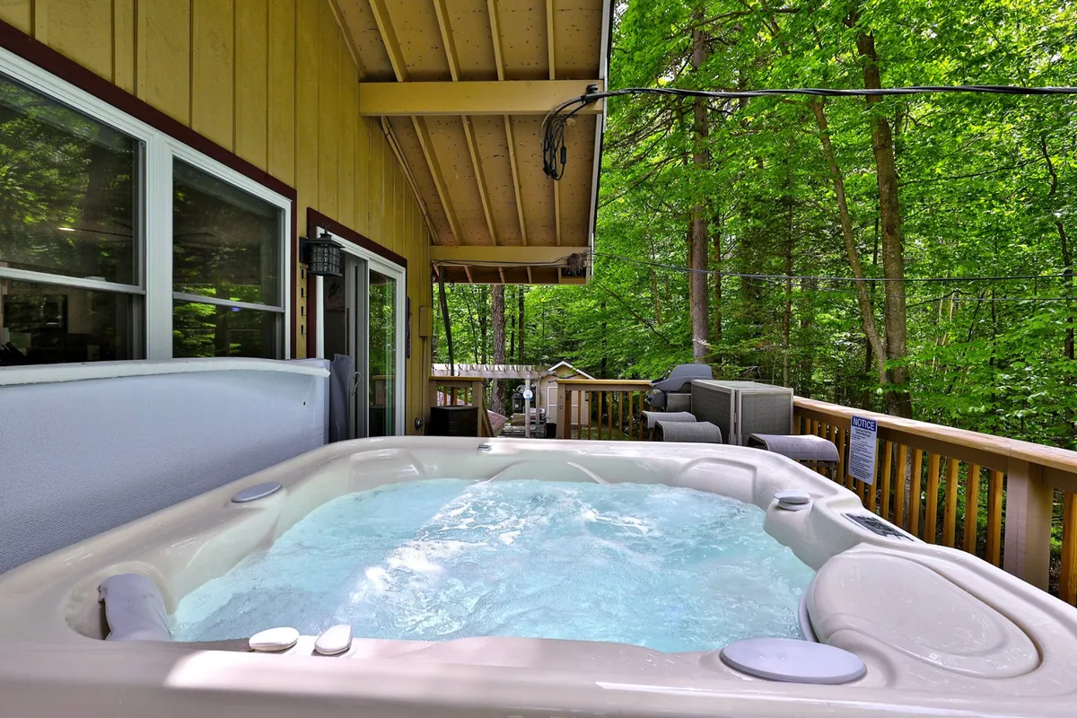This image showcases a hot tub set on a wooden deck surrounded by lush trees, evoking a sense of privacy and immersion in nature. The bubbling water and scenic setting perfectly embody the idea of a wellness retreat after a day’s adventure.