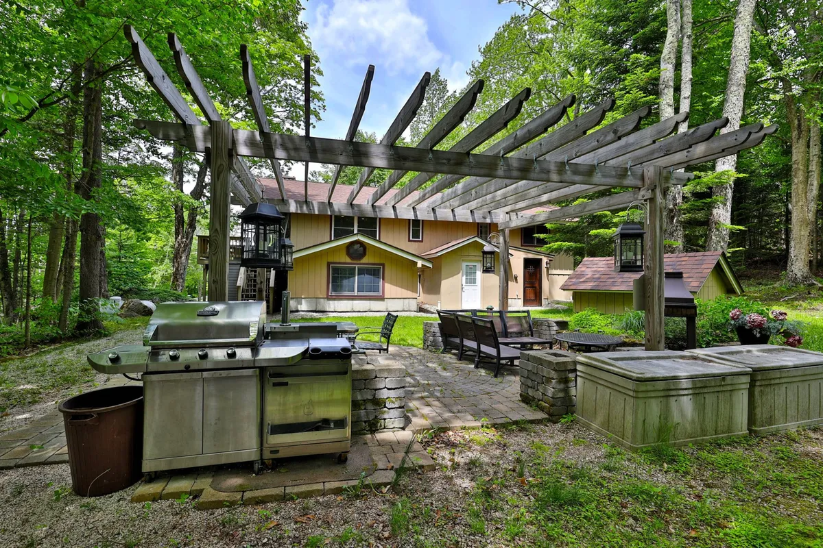 A backyard scene showing a grill and seating area beneath a pergola, framed by thoughtful landscaping. The setup is ideal for barbecues, outdoor dining, and casual gatherings, inviting both relaxation and social connection.