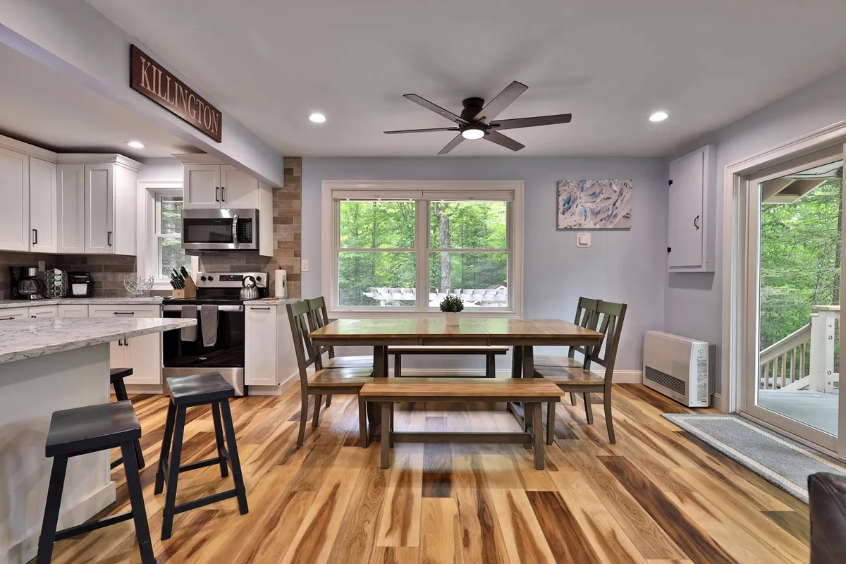 A large dining table sits adjacent to kitchen countertops, with a window view that brings in cozy natural light. This setup evokes a warm environment for family meals, game nights, and group celebrations.