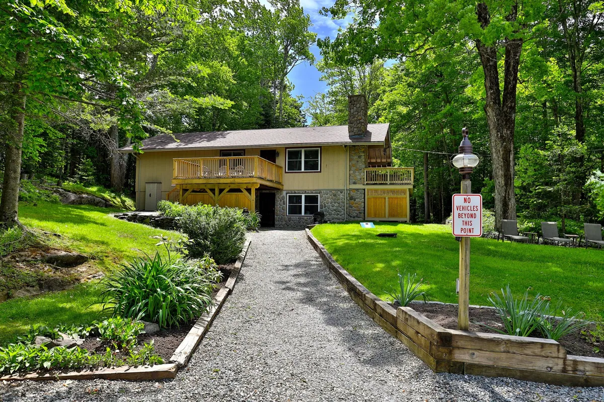A broad exterior view of the house with a clear pathway and lush greenery. The image captures the house’s welcoming approach, with space for large, flat parking and easy access to outdoor amenities.