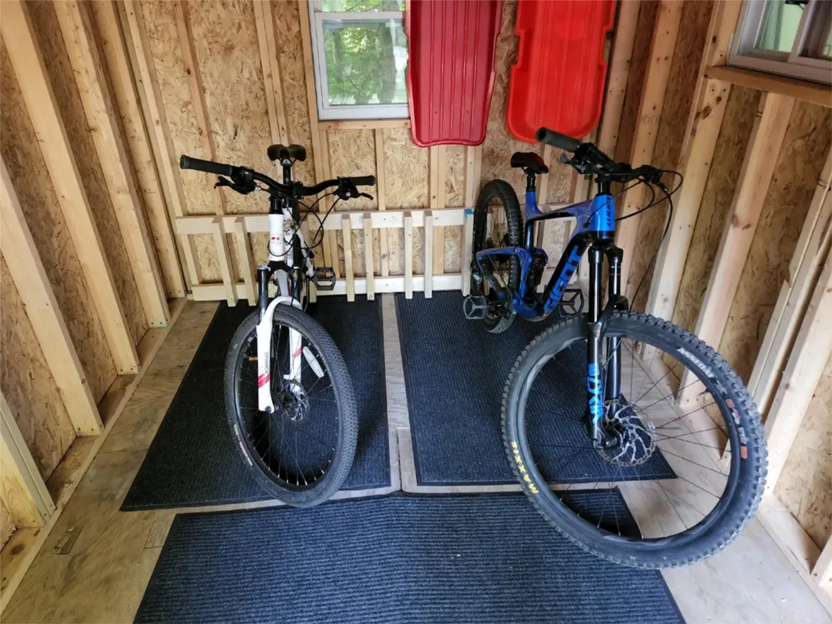 A practical storage area showcasing two mountain bikes and red sleds neatly organized on textured mats. This functional space is well-lit and clearly designed for outdoor adventure gear.