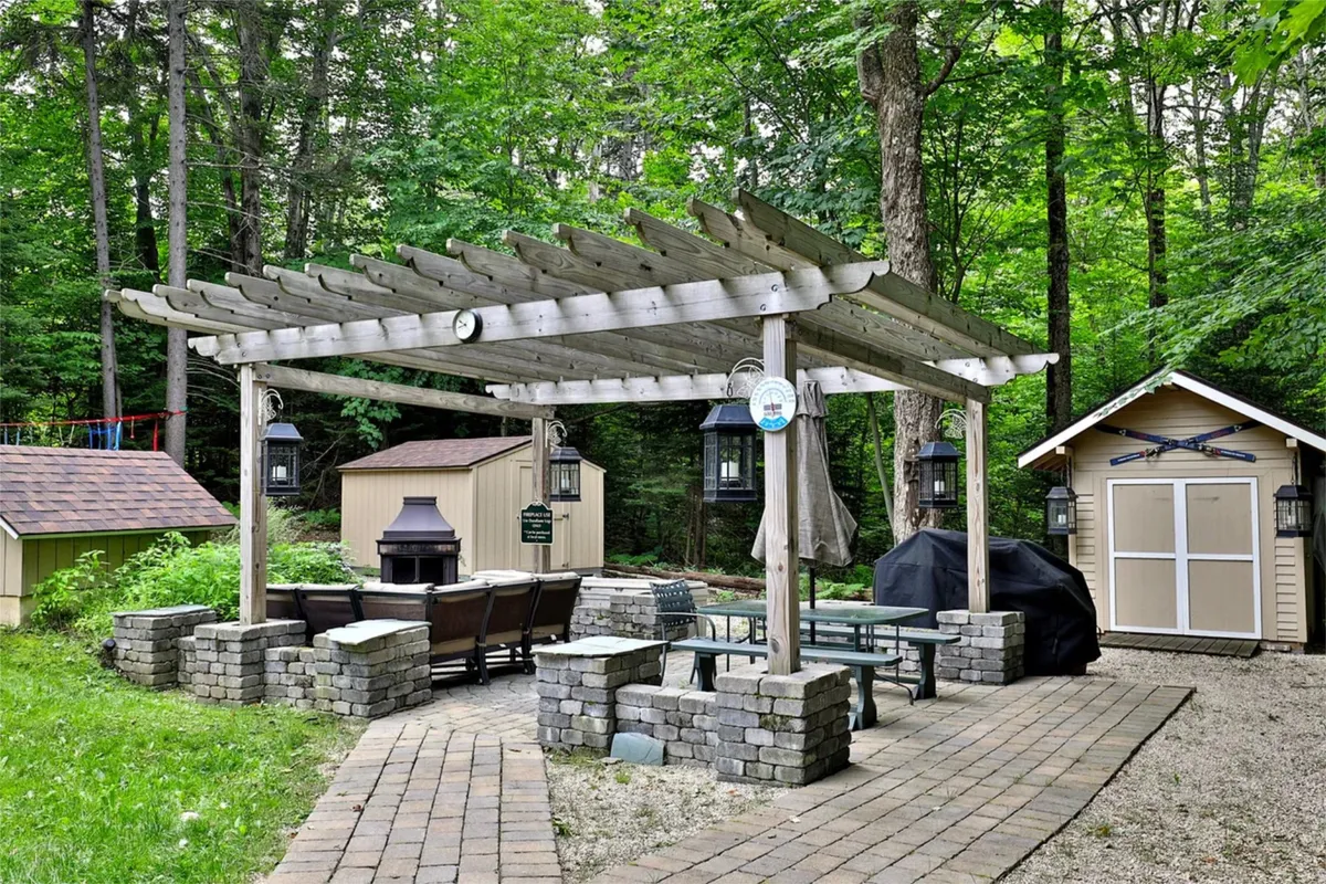 A charming pergola with an outdoor dining area sits beside a stone fire pit and a garden shed, all set against lush greenery. The space is inviting for both social gatherings and peaceful moments by the fire.
